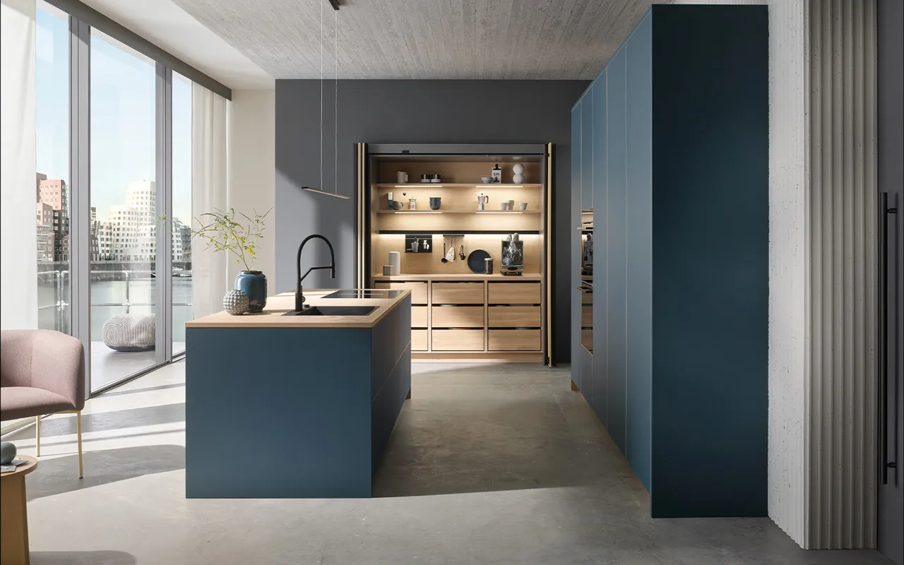 Designküche in Dunkelblau mit heller Holzarbeitsplatte und integrierter Nischenbeleuchtung. Große Fensterfront mit Stadtblick und stilvolle Kombination aus modernen und natürlichen Elementen.